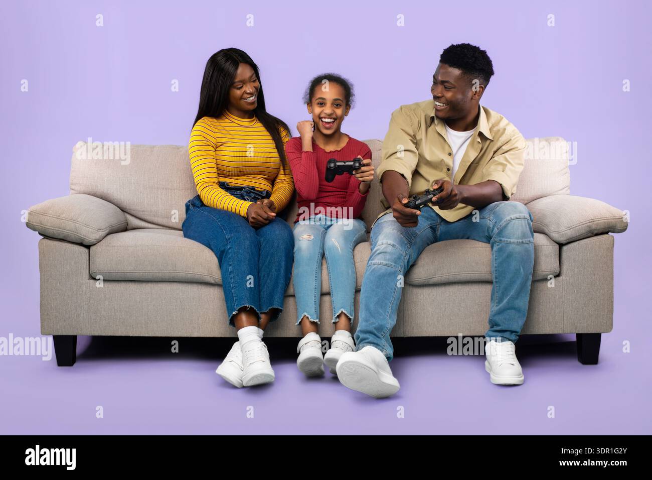 La famiglia gioca ai videogiochi insieme su un divano in un semplice salotto con sfondo viola Foto Stock