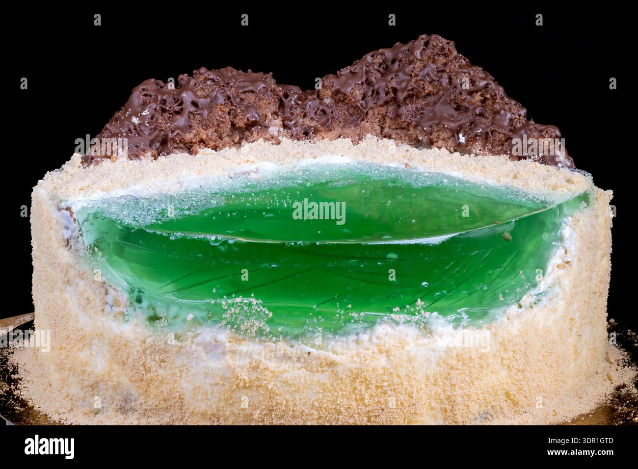 Torta fatta in casa in gelatina verde con picchi di briciole e cioccolato, centro lucido in gelatina illuminata su sfondo nero, spugna di velluto sotto pangrattato sabbioso Foto Stock