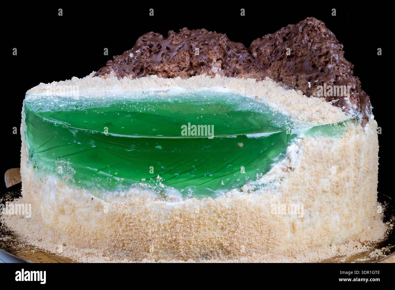 Fetta di torta fatta in casa che rivela gelatina verde e briciole di sabbia, primo piano della sezione tagliata sul piatto da torta, spugna di burro esposta con rivestimento di briciole, panettiere casalingo Foto Stock
