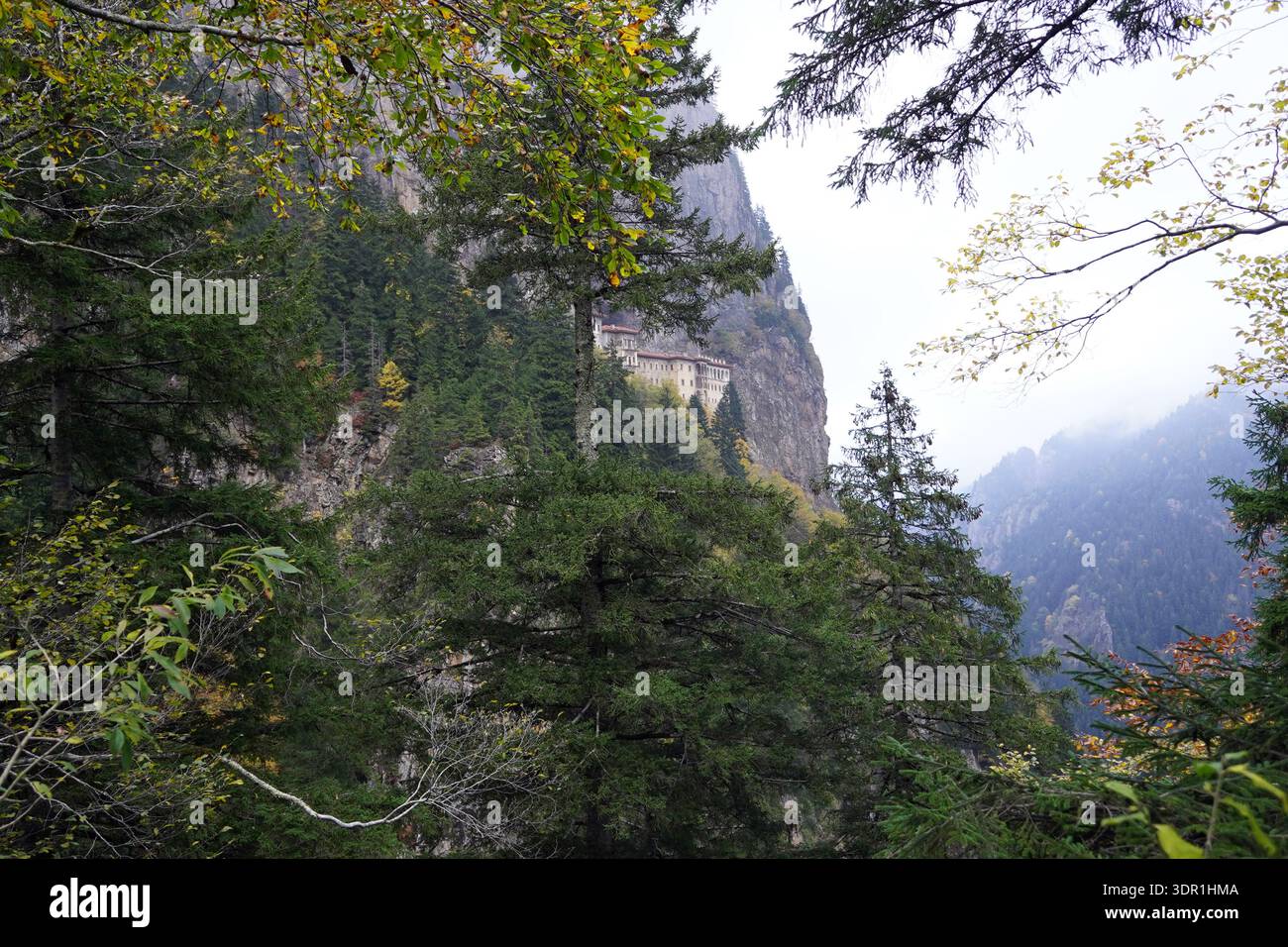L'antico monastero in pietra di Sumela è costruito su una scogliera a strapiombo e annidato tra fitti alberi verdi e dai colori autunnali in una valle di montagna nebbiosa Foto Stock