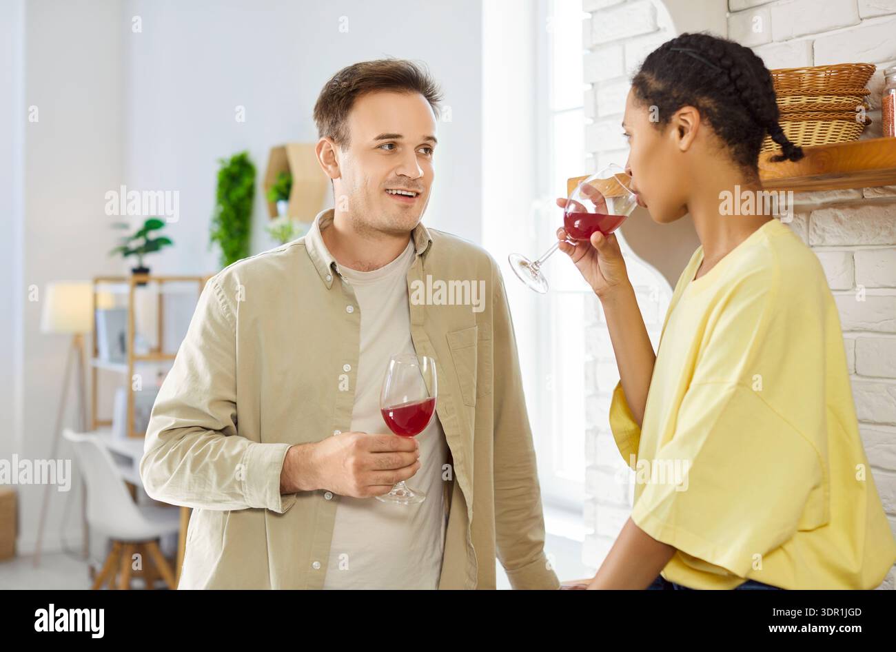 Primo piano di una coppia che tosta bicchieri da vino rosso in un accogliente interno della cucina casalinga Foto Stock