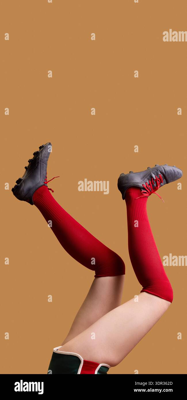 Gambe femminili in calze rosse al ginocchio e tacchetti neri rialzati su sfondo beige. Foto Stock