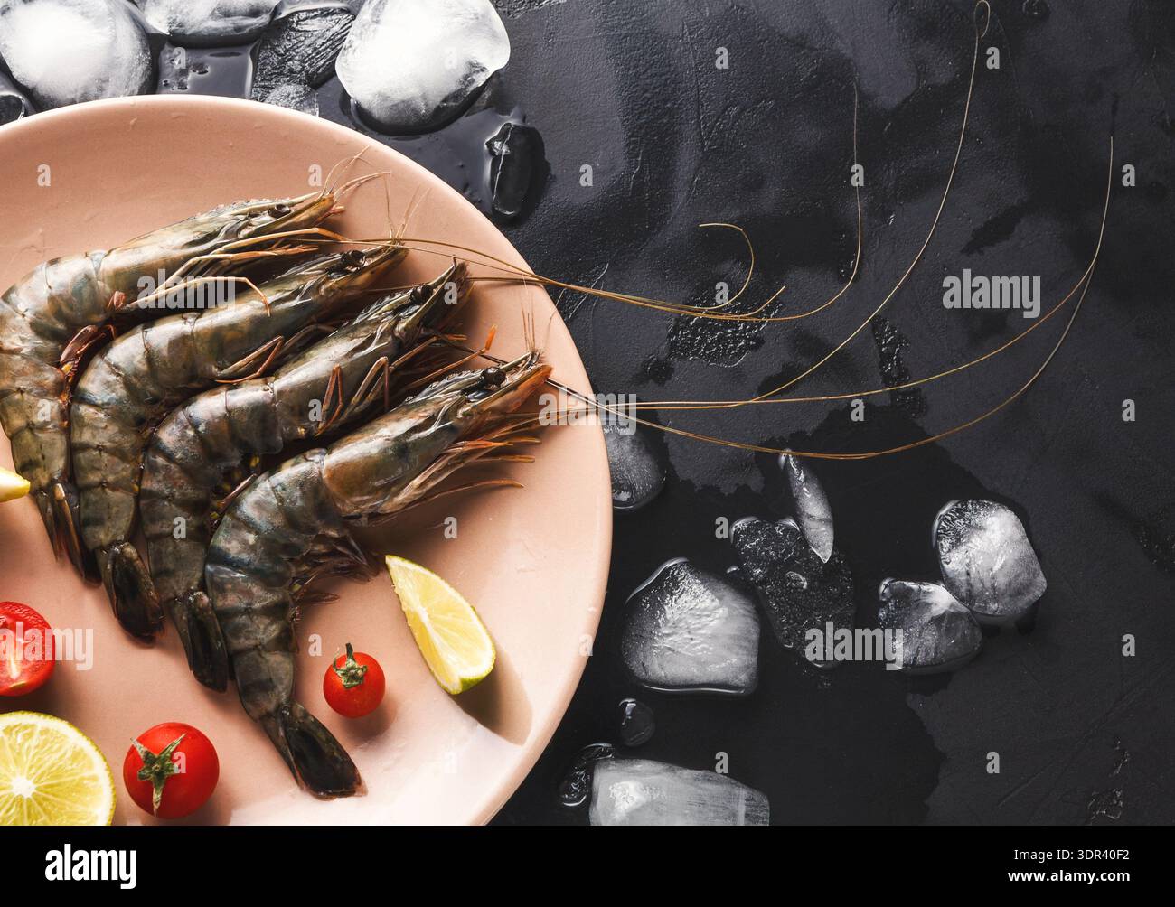 Gamberi freschi sul piatto con spicchi di lime e pomodori ciliegini sulla superficie nera Foto Stock