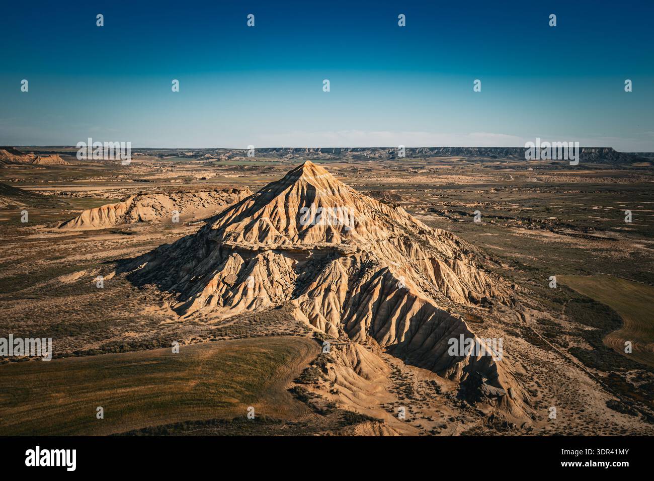 Vista di un paesaggio drammatico e aspro caratterizzato da una montagna prominente e ben definita contro le vaste e aride pianure sotto un cielo azzurro limpido, Bardenas Rea Foto Stock