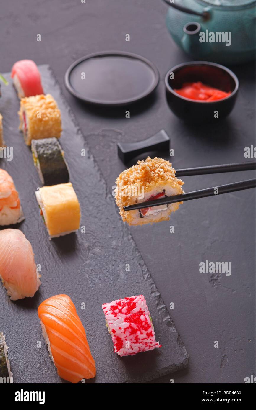 Collezione di sushi su un piatto nero con bastoncini e salse in un ambiente informale Foto Stock