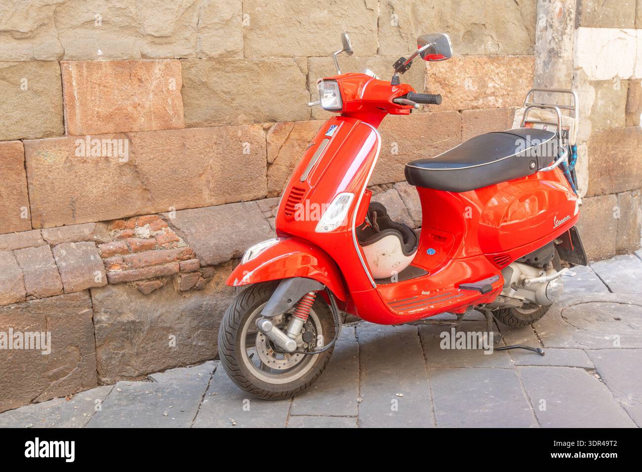 Scooter rosso brillante parcheggiato contro un muro di pietra. Simbolo iconico del trasporto nel Mediterraneo, ideale per il marketing di viaggi, il branding di stili di vita e le vacanze estive Foto Stock