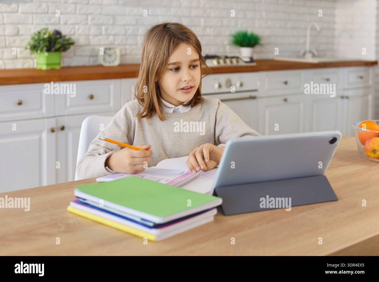 Bambino che completa il lavoro scolastico con un tablet al tavolo della cucina in una casa moderna e accogliente Foto Stock