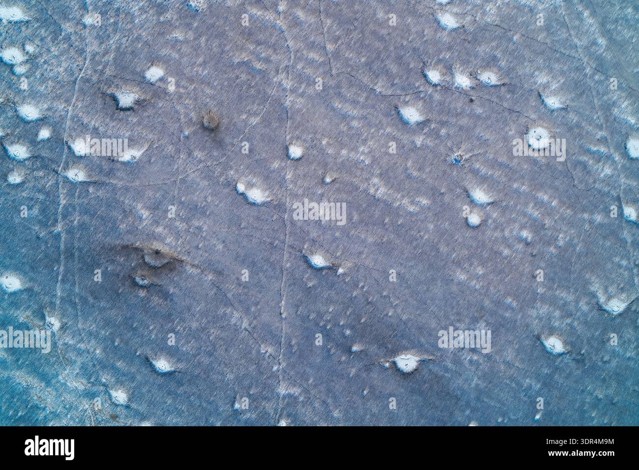 I crateri frastagliati di artiglieria feriscono la superficie ghiacciata di un campo invernale, creando un tragico schema astratto di guerra. Questa cupa vista aerea cattura l'impatto devastante del conflitto sul paesaggio Foto Stock