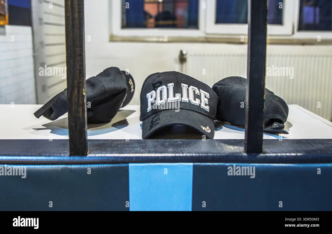 Tre cappellini di polizia neri con testo bianco ricamato in una stazione di polizia dietro le sbarre. Foto Stock