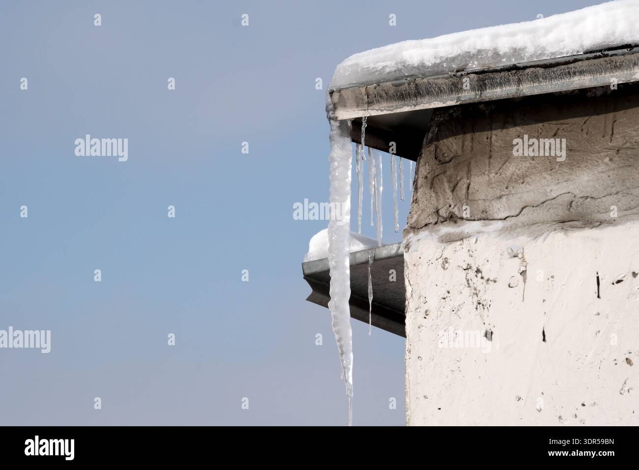 Lunghi ghiaccioli pendono dal bordo di un edificio, catturando la luce del sole e la magia invernale. Foto Stock