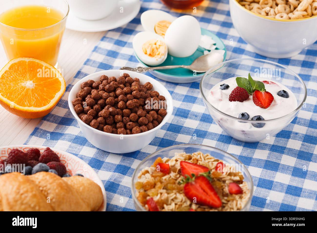 Colazione a buffet con frutta, cereali e yogurt su una tovaglia a scacchi blu Foto Stock