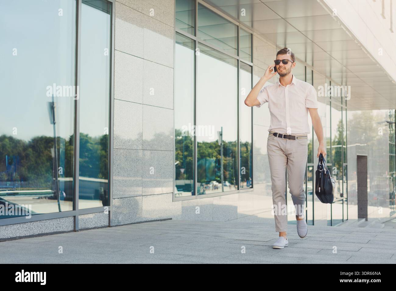 Uomo che cammina su City Street mentre parla al telefono e porta con sé la borsa Foto Stock