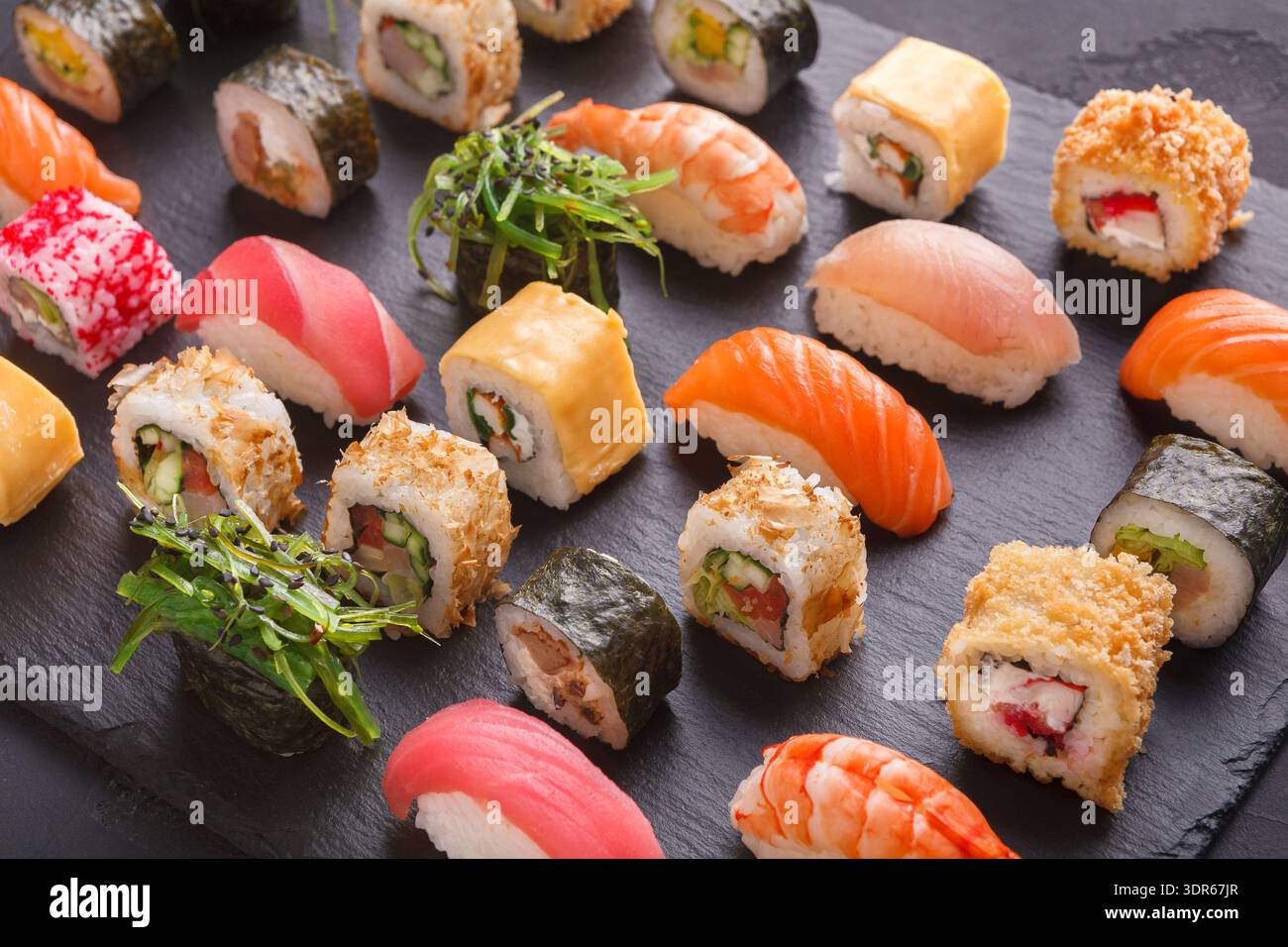 Collezione di sushi disposta su un piatto nero che mostra vari tipi e colori di sushi Rolls Foto Stock