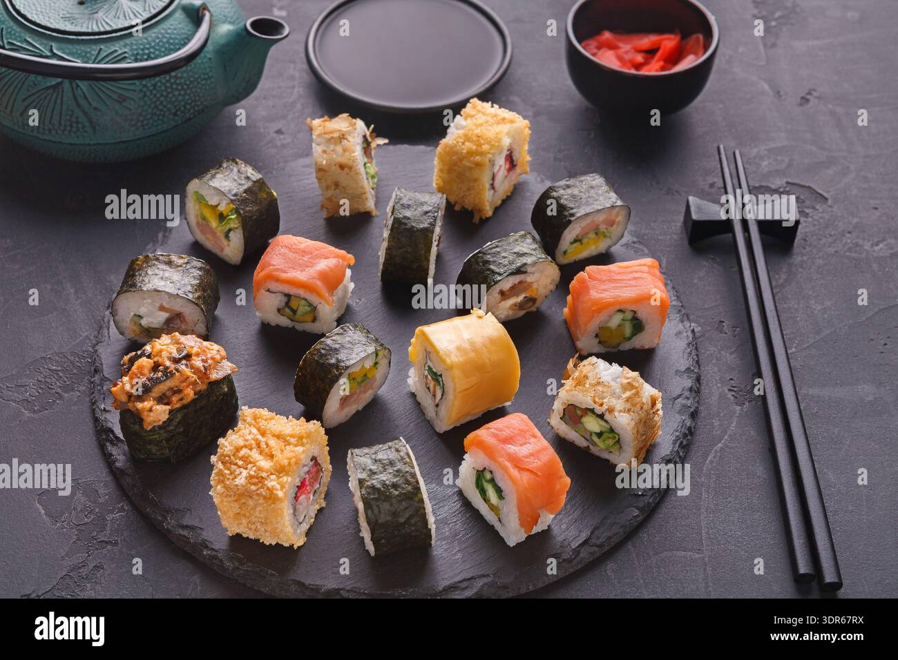 Diversi tipi di sushi sono collocati in un cerchio su una scura tavola di ardesia Foto Stock