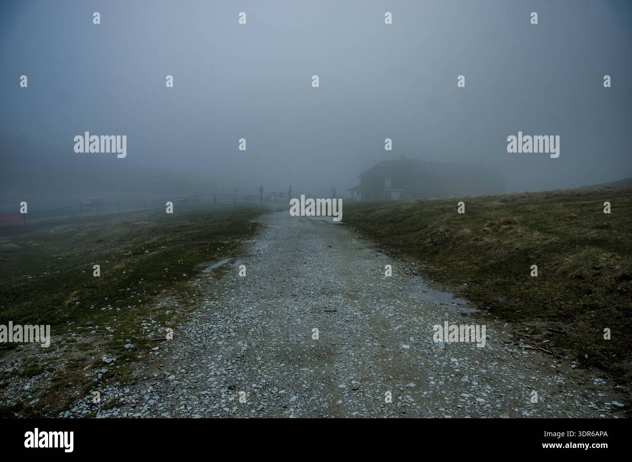 Sentiero ghiaioso che conduce a una sbiadita sagoma di casa tra colline nebbiose e paesaggio coperto Foto Stock