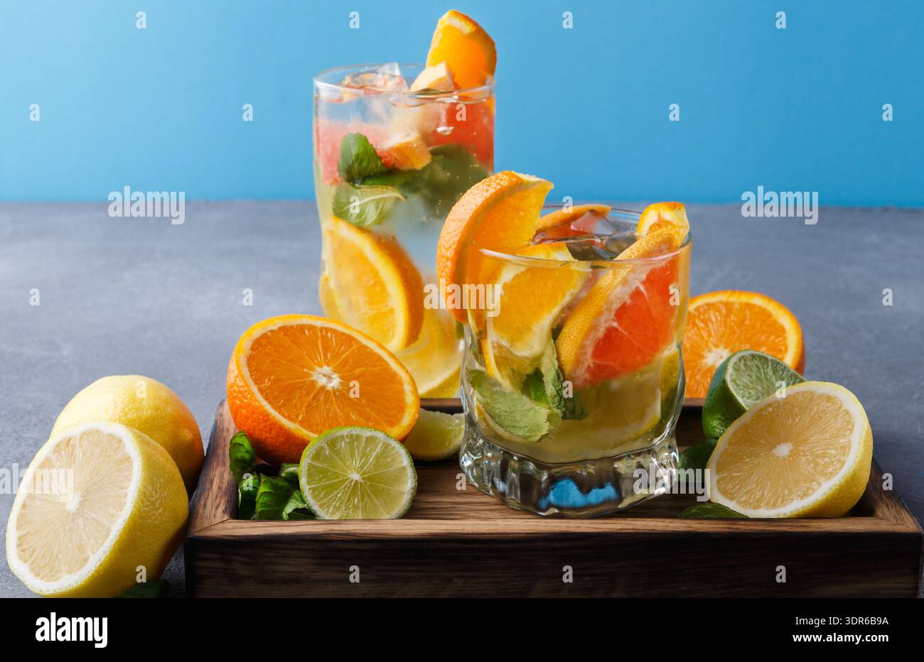 Bevande rinfrescanti alla frutta con limone, arancia e menta su un vassoio di legno su sfondo blu Foto Stock