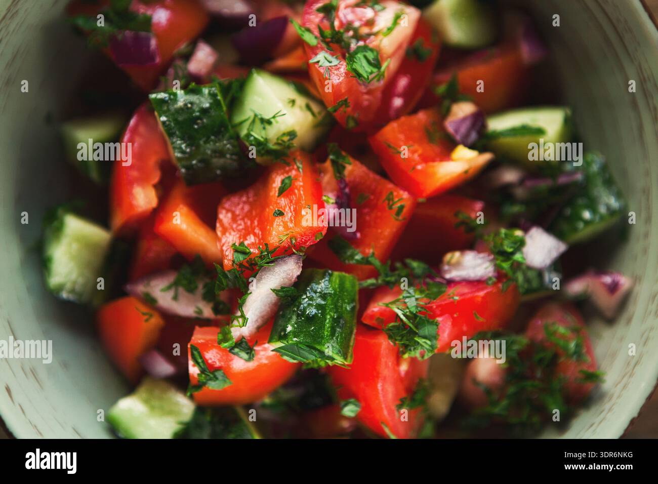 Insalata fresca preparata con pomodori a dadini, cetrioli ed erbe aromatiche in una ciotola durante un pomeriggio soleggiato Foto Stock
