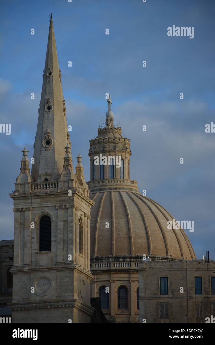 Cupola della chiesa e guglia che si innalzano sopra edifici storici a la Valletta, Malta. Architettura barocca e punto di riferimento religioso nella capitale del Mediterraneo. Foto Stock