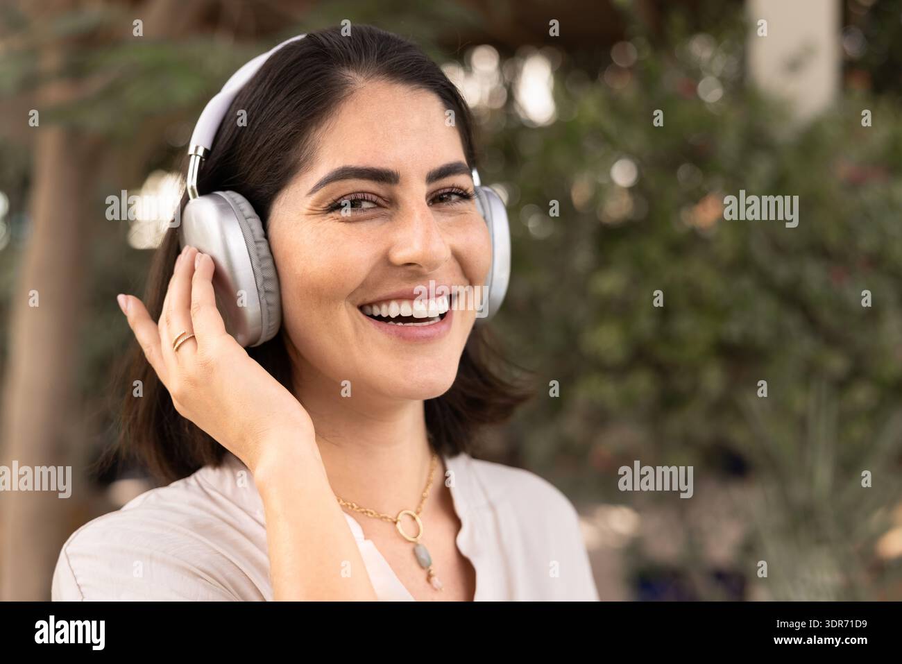 Bella donna latina positiva in cuffie wireless che guarda la fotocamera Foto Stock