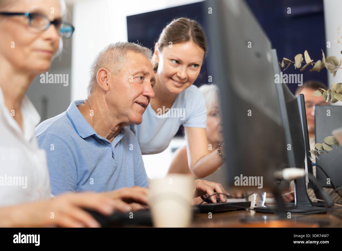 Giovane insegnante di classe informatica per anziani che assiste l'uomo Foto Stock
