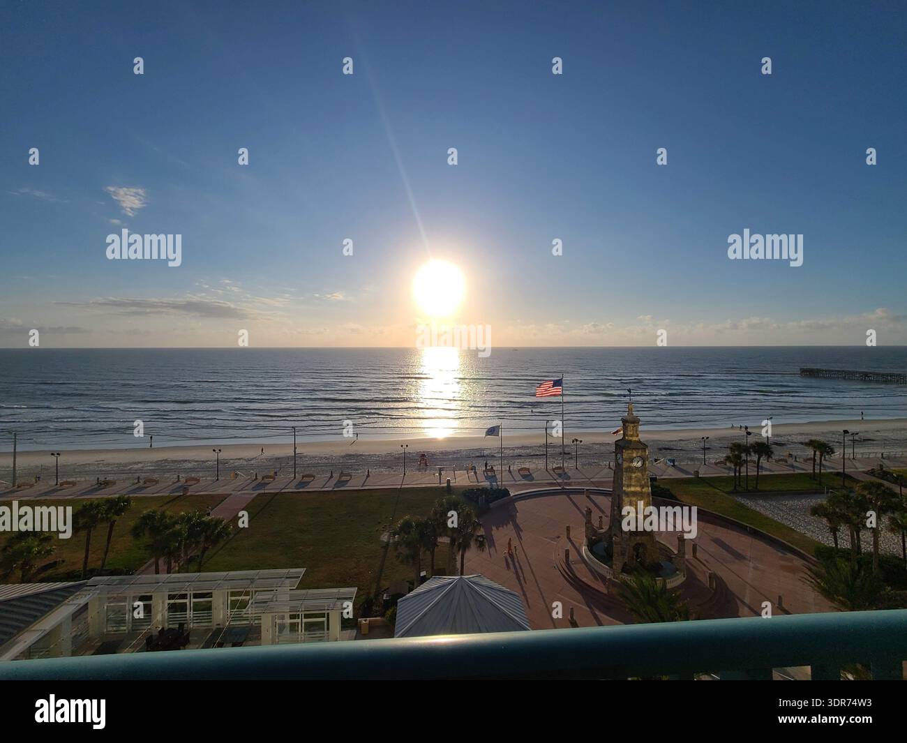 SOLO A USO EDITORIALE - DAYTONA BEACH FLORIDA: ​An ampia vista grandangolare della costa di Daytona Beach con il molo di Main Street e la torre dell'orologio di Coquina. Il sole splende luminoso sull'orizzonte, illuminando l'intero fronte spiaggia, dalle onde ondulate e le sabbie bianche alle lussureggianti palme e alla piazza del lungomare. Uno scatto ad alta prospettiva che cattura le dimensioni e i monumenti iconici di questa famosa destinazione di vacanza in Florida. - Immagine stock catturata con smartphone