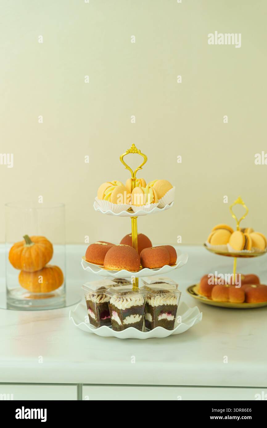 Un'esposizione di dessert mostra tre livelli di dolci, tra cui biscotti e tazze con strati di panna. Nelle vicinanze si trova una zucca, che si aggiunge all'atmosfera festosa Foto Stock