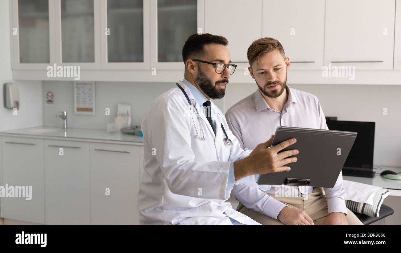 Medico di sesso maschile che discute documento medico su appunti con il paziente giovane Foto Stock