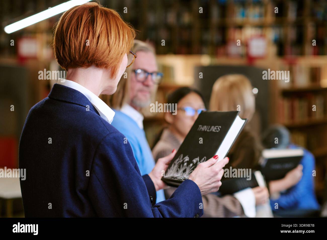 Donna caucasica di mezza età che tiene il libro mentre è in fila in ambiente biblioteca Foto Stock
