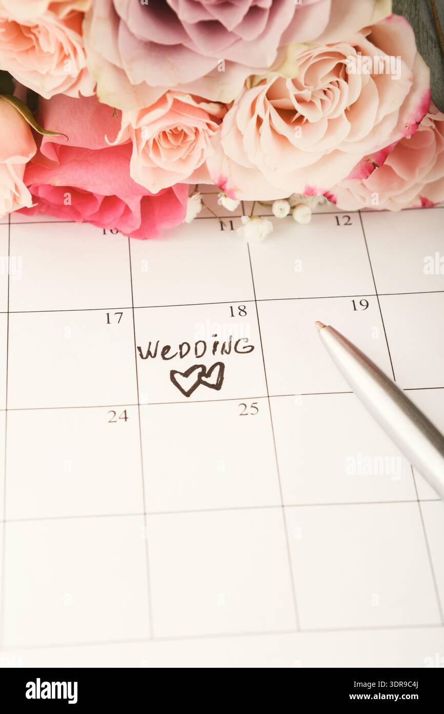 Pianificazione di un matrimonio con un calendario, fiori e una penna in una raccolta di dettagli Foto Stock
