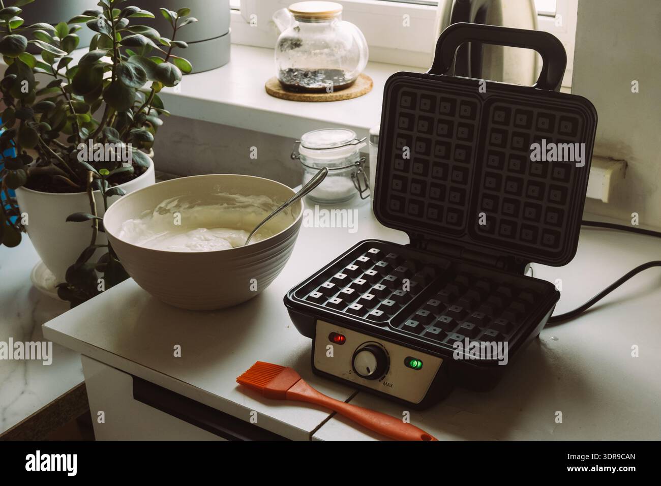 Scena di preparazione dei waffle da cucina con recipiente, spazzola in silicone e ferro da stiro vuoto per cialde per impaginare ricette, intestazione del blog alimentare e design dello sfondo Foto Stock