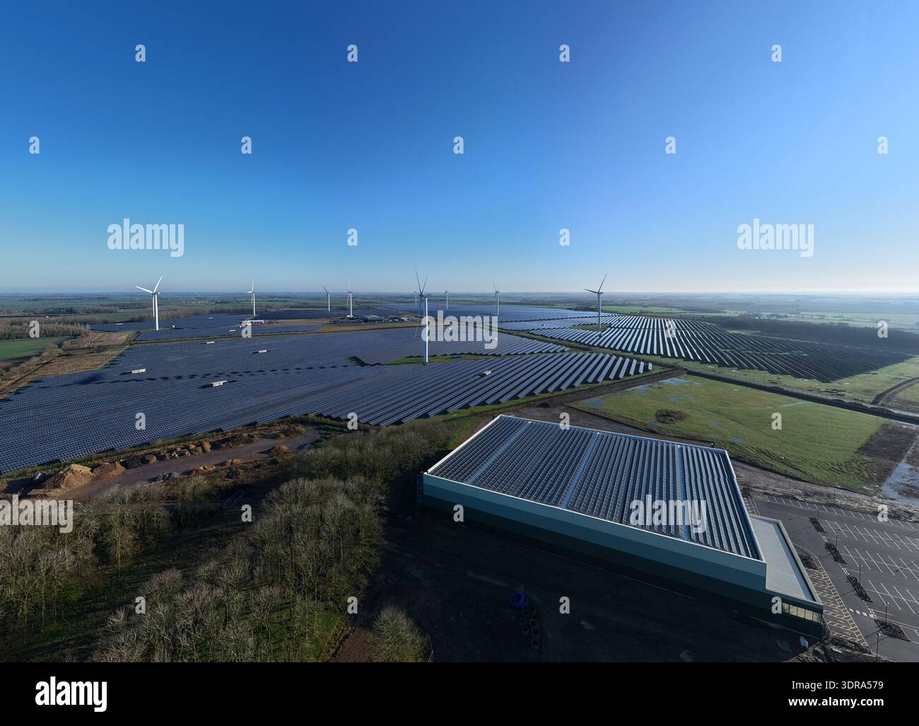 Vista aerea della luce del sole che si riflette sui pannelli solari e sulle turbine eoliche contro il cielo blu profondo, Chelverston, Wellingborough, Regno Unito. Foto Stock