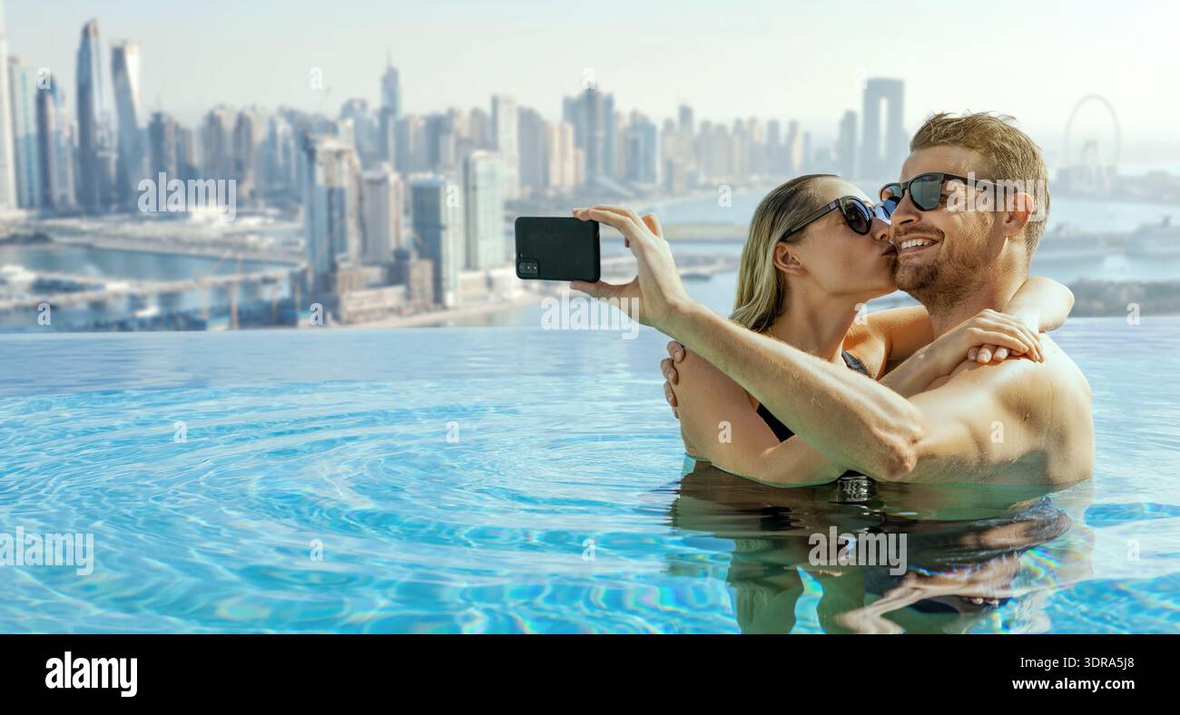 Coppia romantica che scatta un selfie nella piscina a sfioro sul tetto con lo skyline di Dubai sullo sfondo. banner con spazio di copia Foto Stock