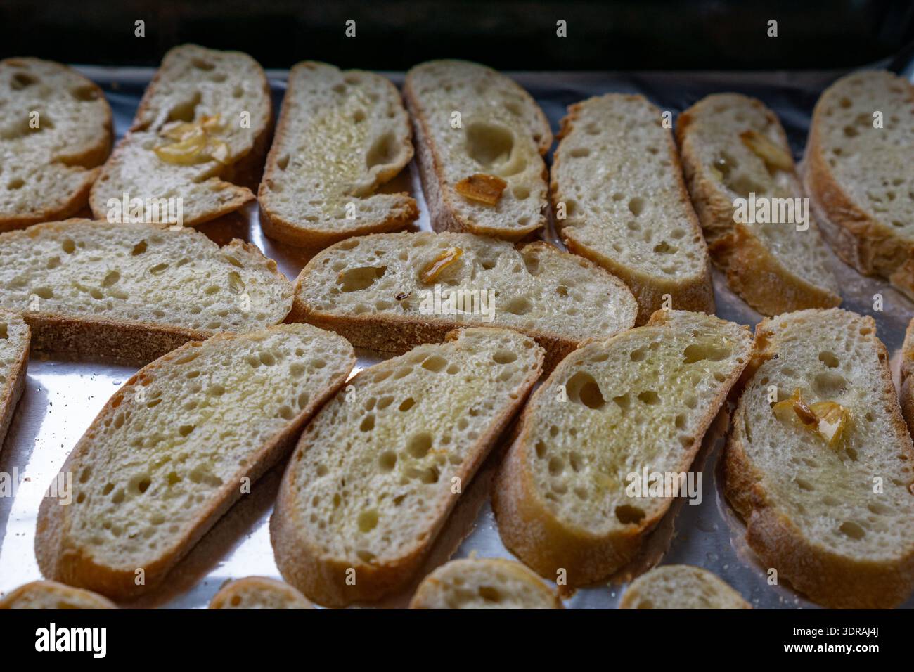Primo piano di fette di baguette spazzolate con olio d'oliva e ricoperte con piccoli pezzi d'aglio. Foto Stock