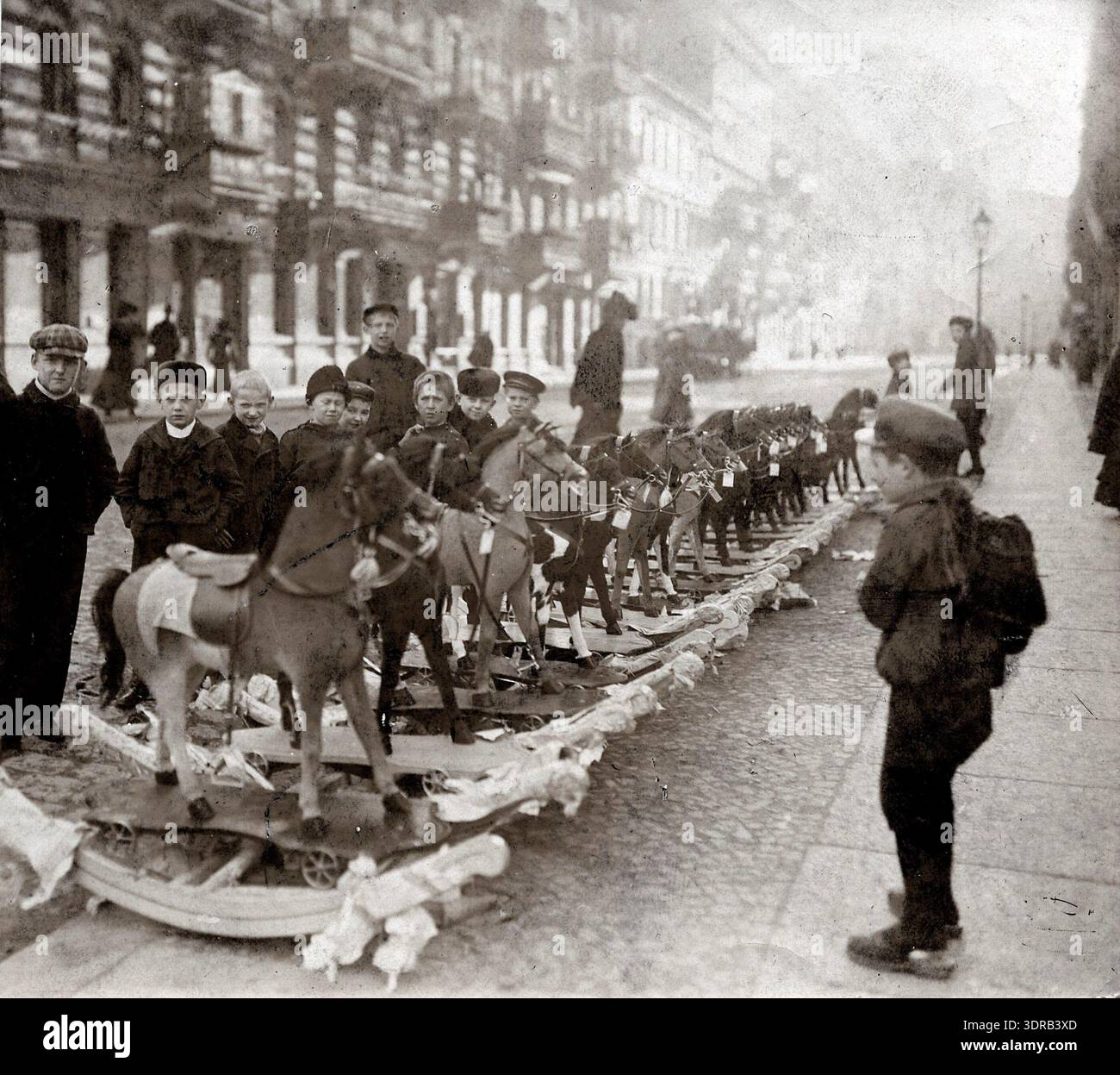 Questa fotografia del 1921 di otto Haeckel mostra i bambini che osservano le vendite di giocattoli durante il periodo natalizio a Berlino, in Germania. I ragazzi sono particolarmente interessati ai cavalli a dondolo. L’immagine illustra il commercio urbano dei primi anni del Novecento, la vendita al dettaglio stagionale, gli interessi dei bambini, la produzione di giocattoli, l’attività del mercato pubblico, e la cultura dei consumatori per le vacanze, che fornisce informazioni storiche sulla vita urbana post-bellica e sulle pratiche di svago infantile europee. Foto Stock
