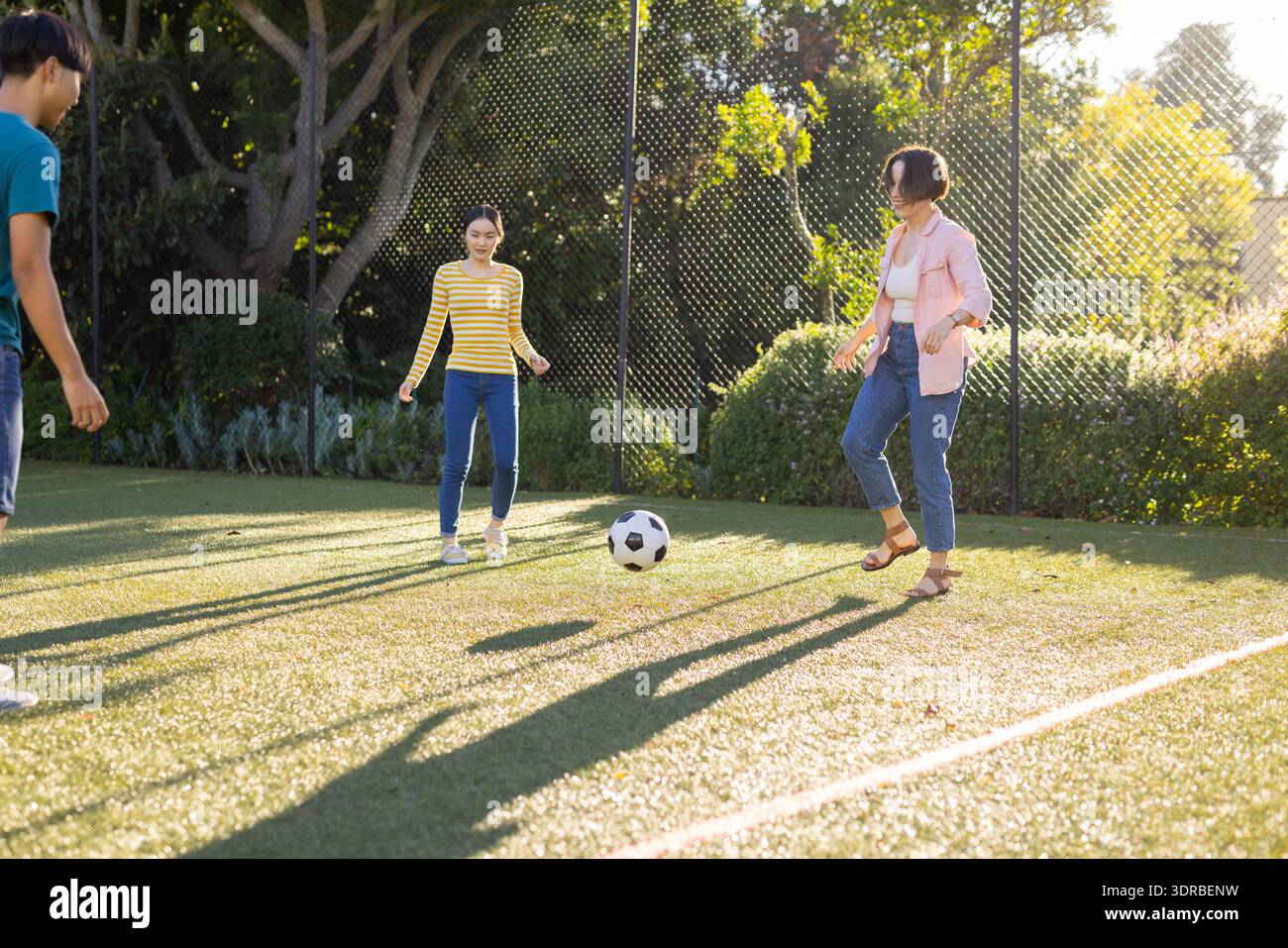Giocando a calcio sul campo, la famiglia asiatica si diverte a praticare attività all'aperto insieme nel parco Foto Stock
