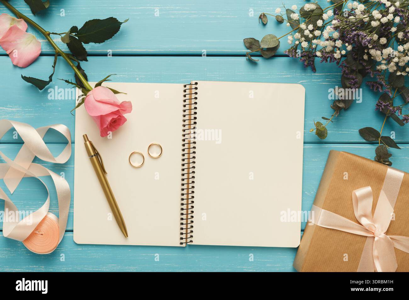 Collezione di articoli su un tavolo blu con fiori rosa, anelli d'oro e una confezione regalo Foto Stock