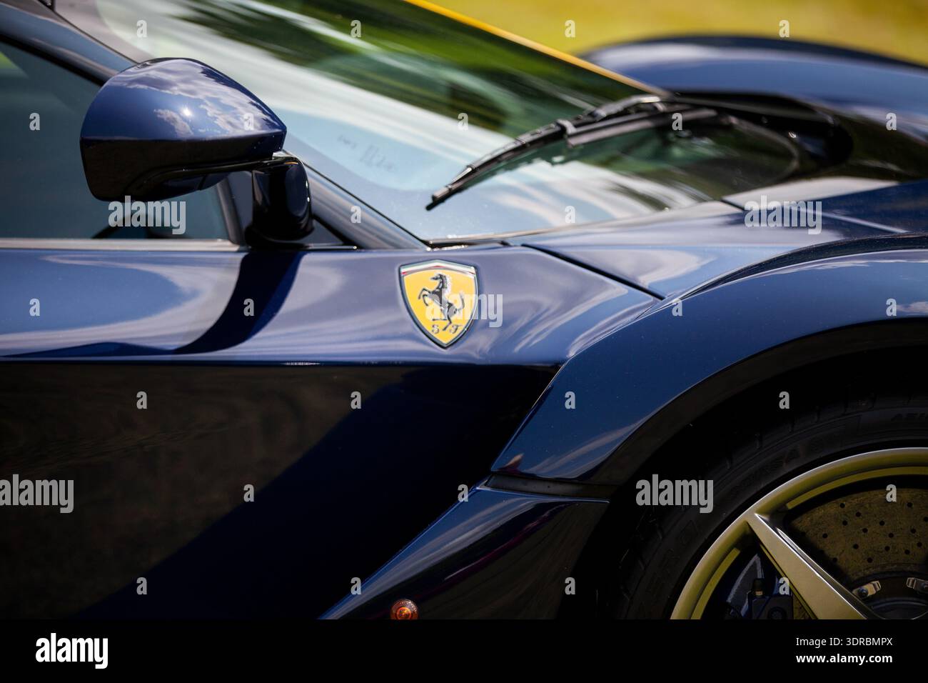 Primo piano di un'auto sportiva Ferrari blu che mostra il distintivo del cavallo, lo specchio laterale e la ruota anteriore, con riflessi sulla carrozzeria lucida. Foto Stock