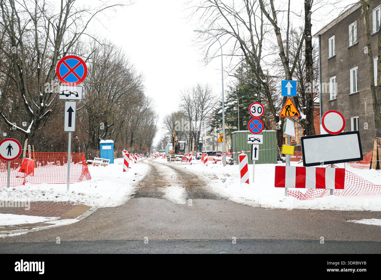 Lavori stradali su strade innevate della città con segnali stradali e barriere. Cantiere urbano invernale con deviazioni, segnali di avvertimento e accesso limitato. Foto Stock