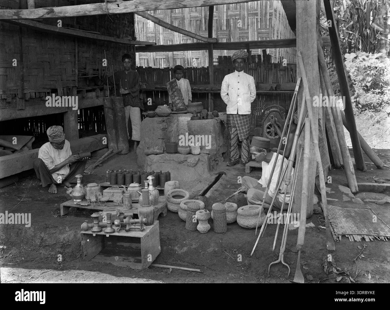 Questa fotografia del 1910 di Jean Demmeni raffigura uomini indonesiani che lavorano in un laboratorio di fabbro a Soengai Poear, Sumatra, Indonesia, ex Indie Orientali olandesi. L'immagine documenta le pratiche, gli strumenti e le tecniche tradizionali di lavorazione dei metalli utilizzate all'inizio del XX secolo. Il laboratorio riflette l'artigianato artigianale, la cultura industriale locale e il ruolo della lavorazione dei metalli nella vita della comunità e nell'attività economica di Sumatra. Foto Stock