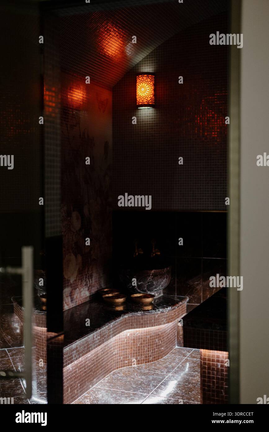 L'interno di un hammam tradizionale con panche in marmo e una lampada da parete decorativa. Un'area relax hammam con lettini in marmo riscaldati e un ornato Foto Stock