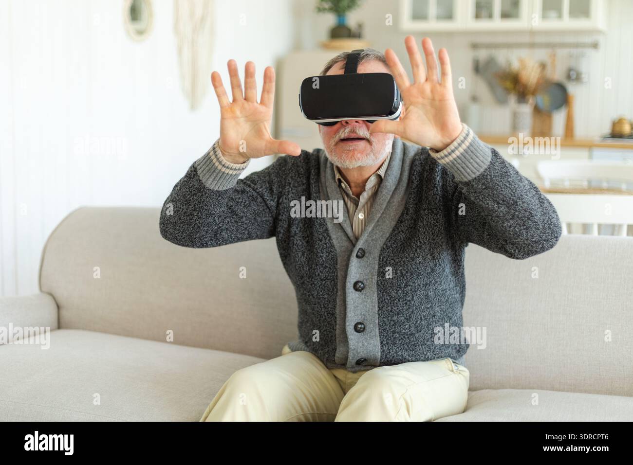 Uomo anziano entusiasta che indossa a casa occhiali VR metaversi con realtà virtuale. Nonno che tocca l'aria durante la realtà virtuale Foto Stock