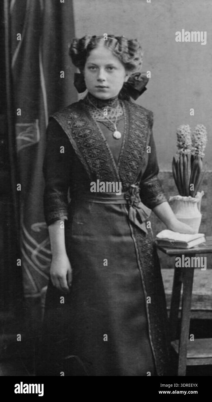 Questa fotografia di Max Holdt raffigura una giovane donna a Pirna intorno al 1900, che indossa un'acconciatura di gatto tipica del periodo della Belle Époque. L'immagine mette in evidenza moda, acconciatura e indicatori sociali di ricchezza basati sulla residenza urbana. Era raro trasferirsi in una grande città, riflettendo la struttura sociale, la mobilità e la classe sociale nella Germania dell'inizio del XX secolo. La strada Gartenstraße 31 è nota come il luogo della fotografia, documentando la vita quotidiana e la presentazione personale durante quell'epoca. Foto Stock