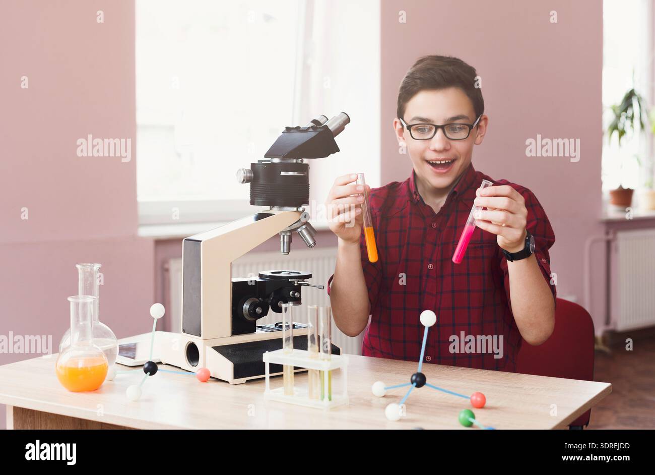 Boy conduce un esperimento con un microscopio e provette colorate in aula Foto Stock