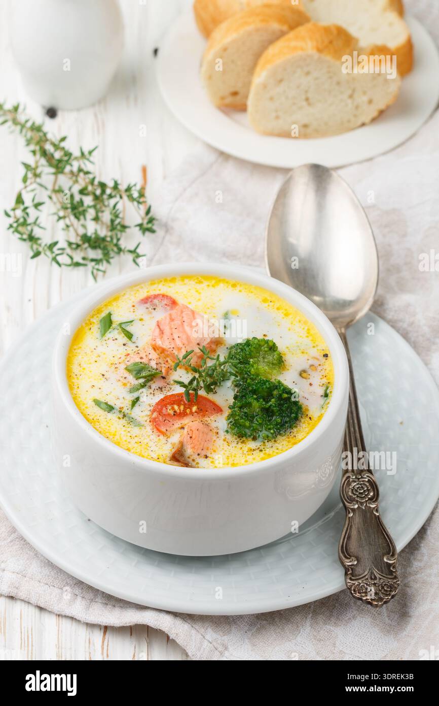 Salmone zuppa cremosa con verdure - patate, carote, pomodori e broccoli in una ciotola bianco luminoso su un tavolo di legno Foto Stock