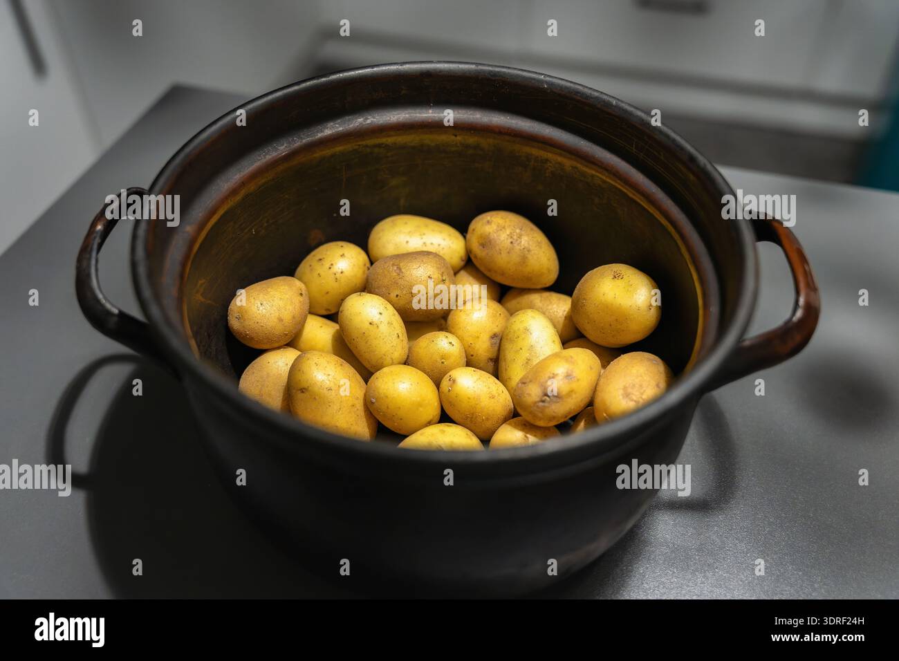 Patate gialle intere non sbucciate all'interno di una pentola di cottura in metallo condita con patina visibile Foto Stock