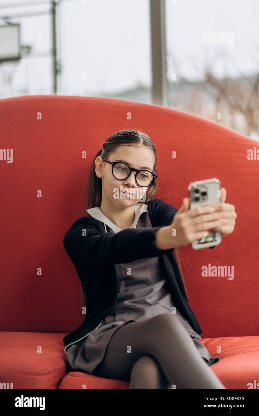 Ragazza adolescente che scatta selfie sul divano rosso sentendo l'effetto di inferiorità dello schermo dal confronto tra i social media e filtri di bellezza per smartphone con identità digitale Foto Stock