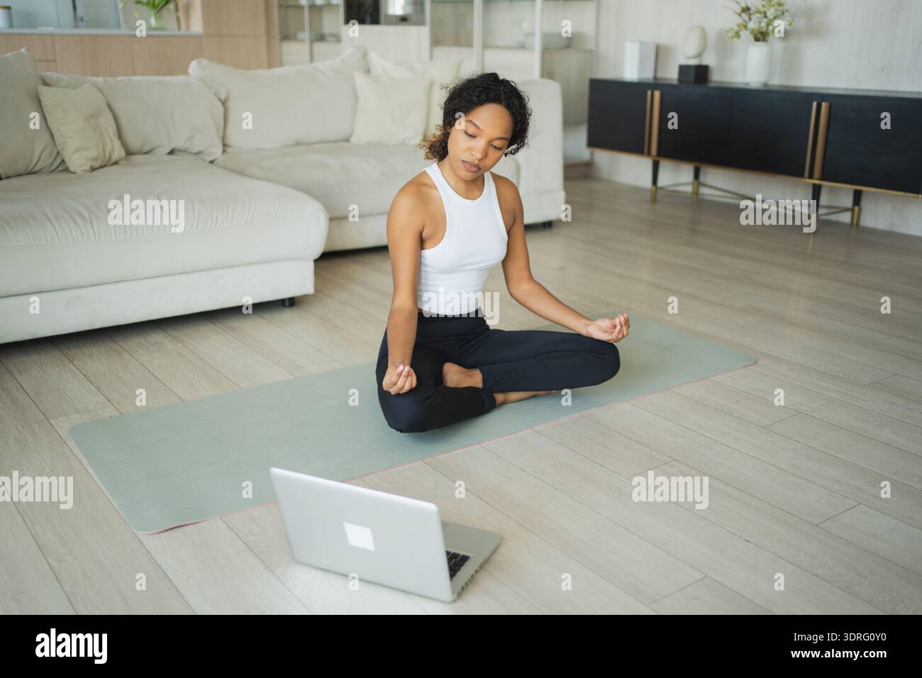 Meditazione sulla consapevolezza dello yoga online. Donna africana che pratica yoga con lezioni online su laptop a casa. Donna seduta nel loto Foto Stock