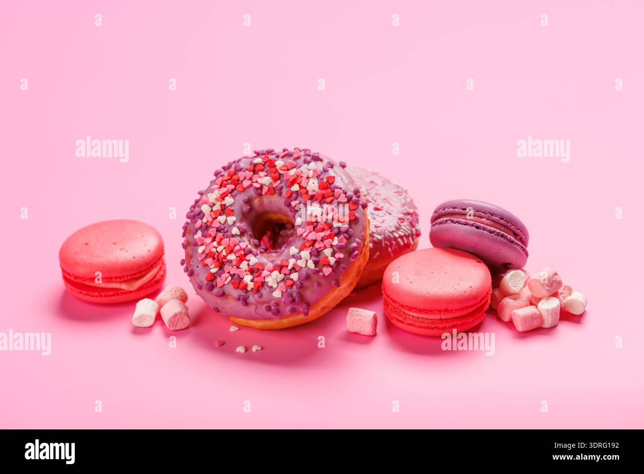 Una disposizione accattivante di macaron colorati e ciambelle su sfondo rosa pastello Foto Stock