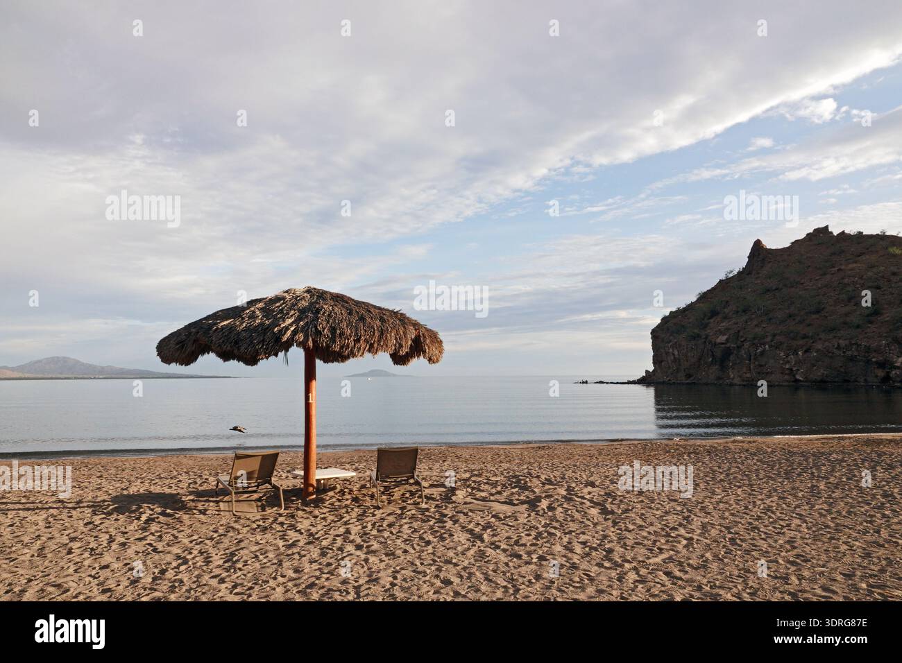 Un ombrellone con tetto in paglia ombreggiano i turisti su una spiaggia di Nopolo, Baja, Messico, vicino alla città di Loreto. Foto Stock