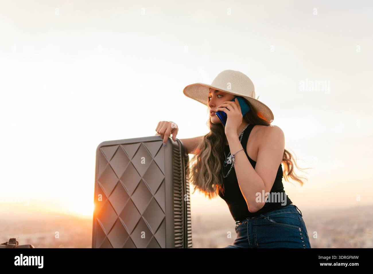 La donna viaggiatrice, che ha la sua borsa da viaggio accanto a lei, sta parlando al telefono. Foto Stock